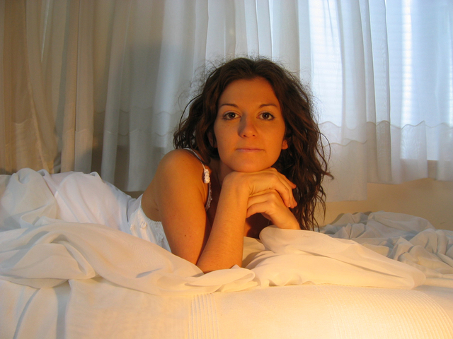 Žena v posteli, záclony, priamy pohľad